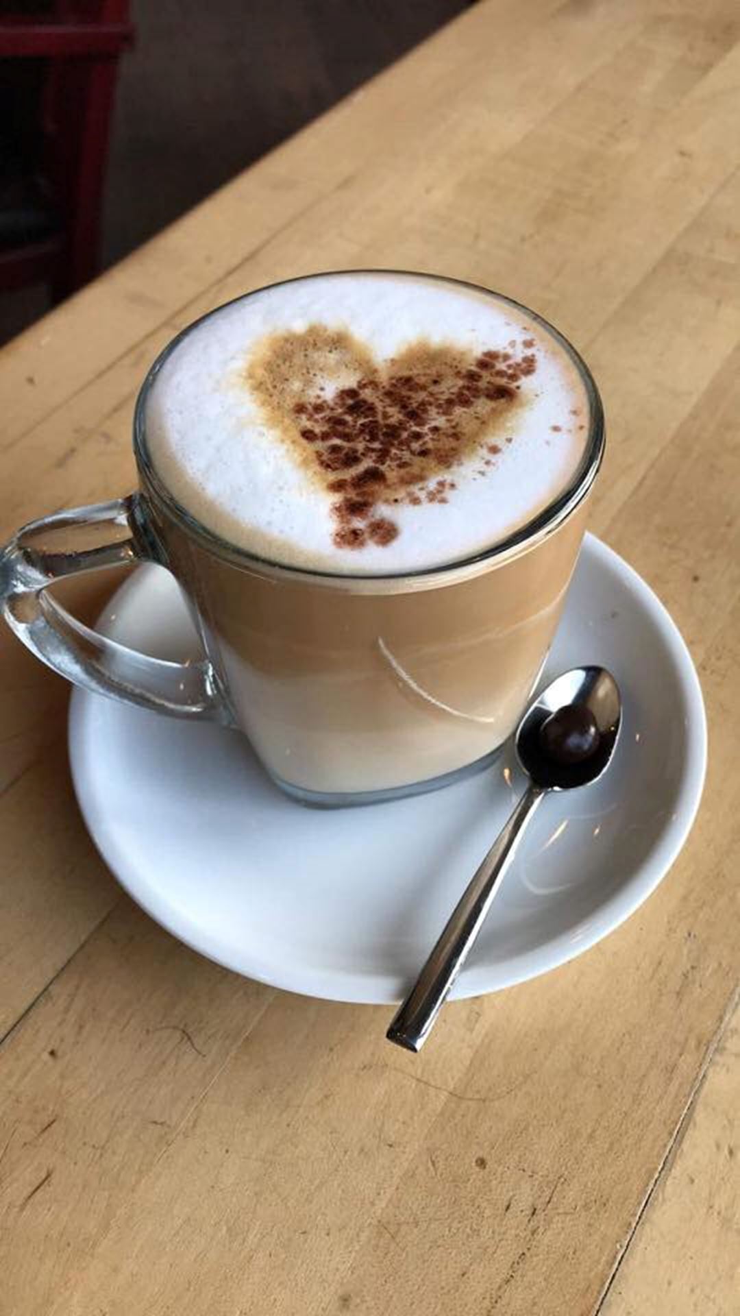 Café latté avec un coeur fait au pochoir en cacao sur une mousse de lait blanche.