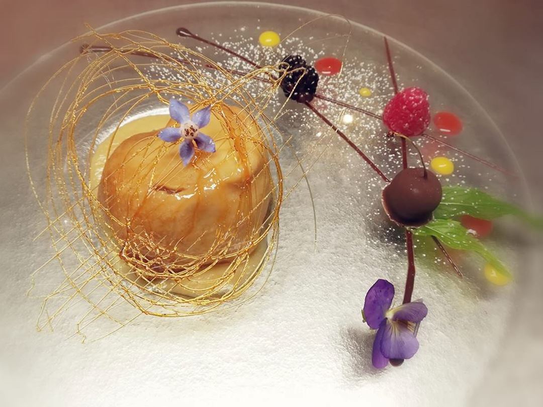 Crêpe aux pommes accompagnées d'une sauce au caramel servie dans une assiette en verre transparent.