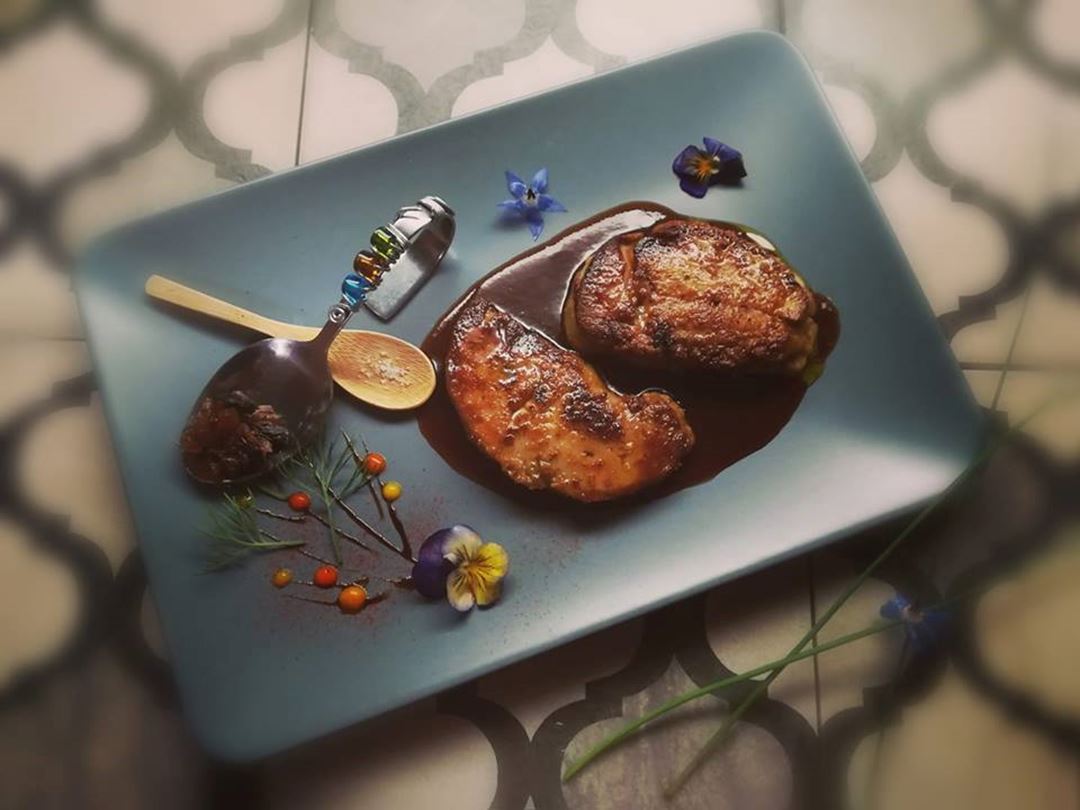 Viande servie dans une assiette rectangulaire noire et accompagnée d'un filet de sauce.