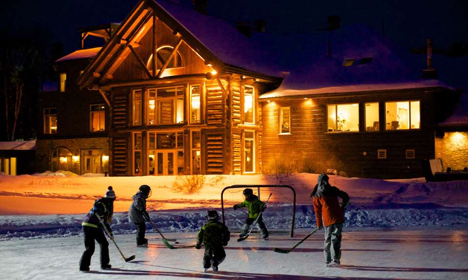 Enfants qui jouent au hockey devant l'Auberge du Lac Taureau durant l'hiver