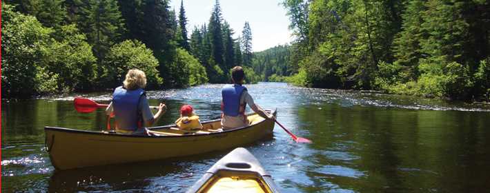 Famille qui fait du canot sur une rivière près des montagnes l'été
